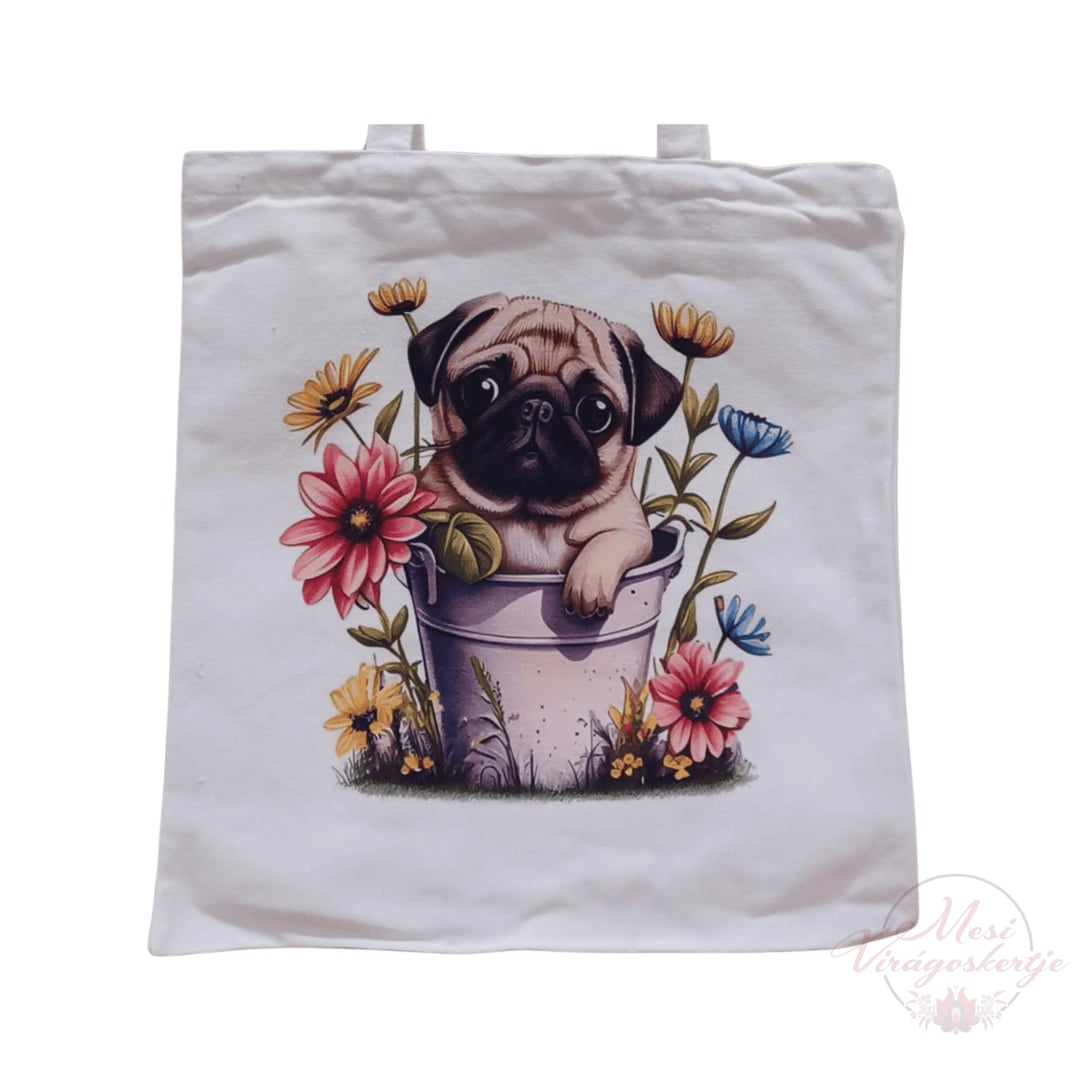 Fehér vászontáska színes illusztrációval: egy kiskutya ül egy virágcserépben, körülötte rózsaszín, sárga és kék virágok. A design alján „Mesi Virágoskertje” felirat látható.